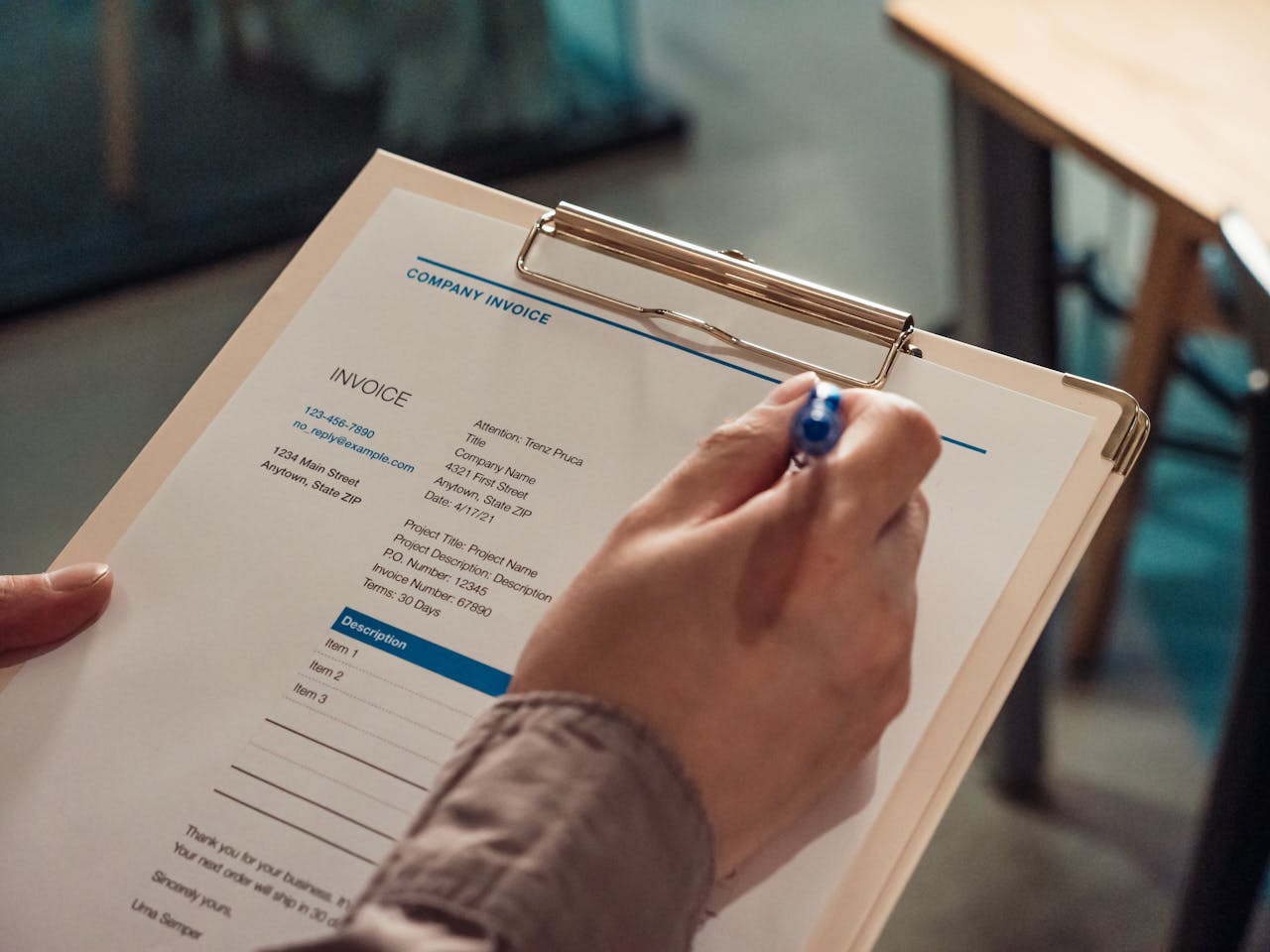 Person's hand holding a company invoice on a clipboard with a pen.