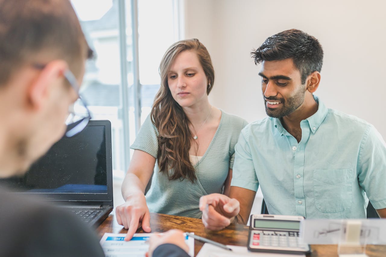 Young couple consulting with a financial advisor using a calculator and documents in a bright office setting.